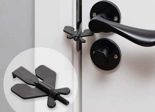 A portable door lock in the jamb of a white door with dark metal hardware.