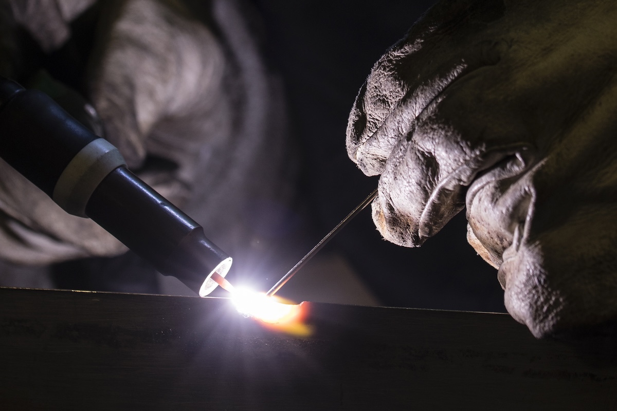 A welding wears thick protective gloves while completing a TIG welding project. 