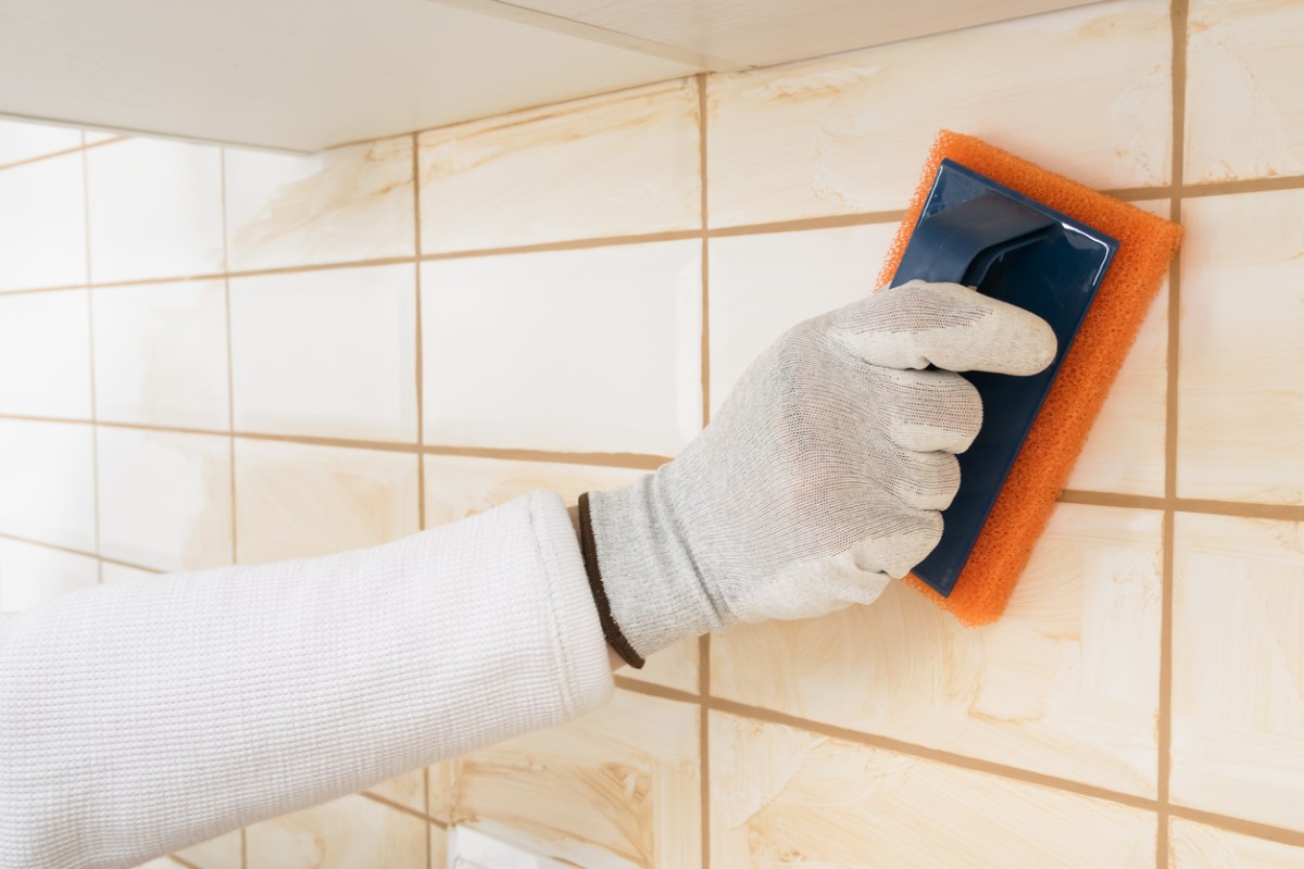 Gloved hand rubbing grout into wall tile joints