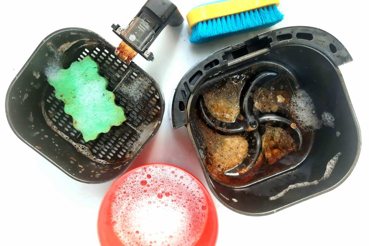 Air fryer basket taken apart and being cleaned on a white background