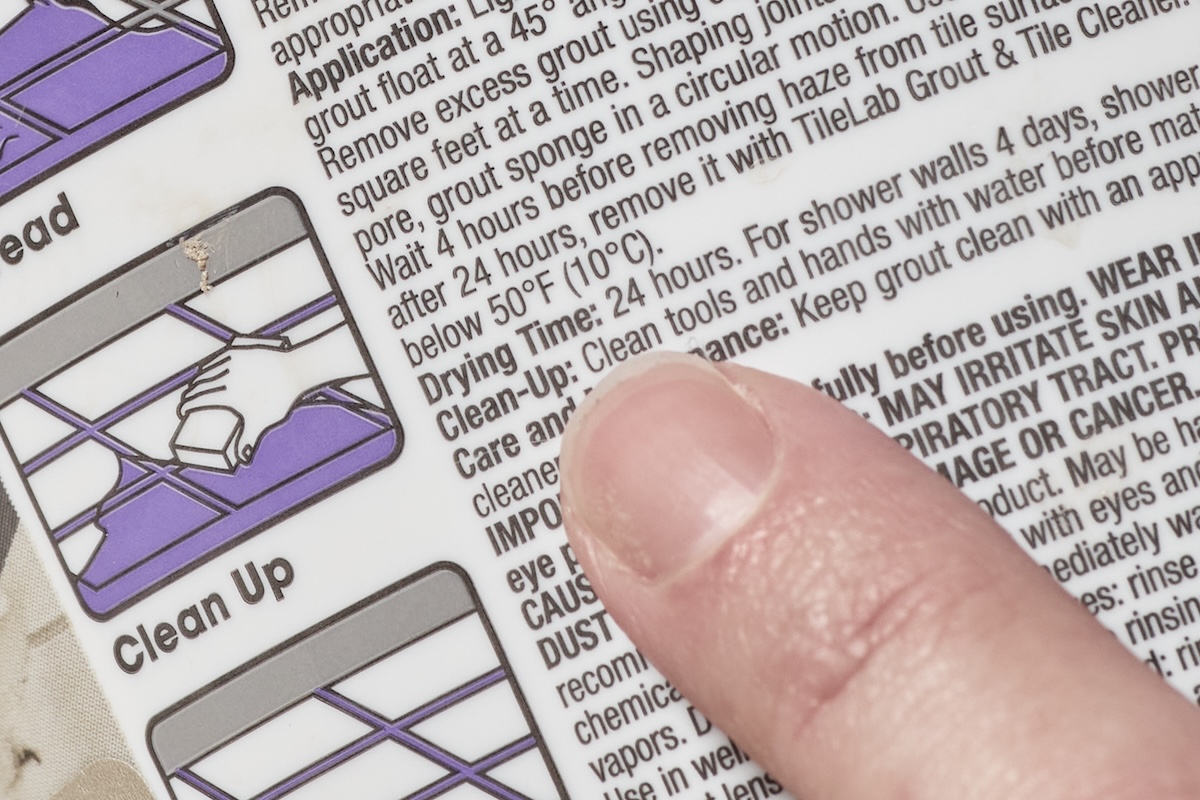 Finger points to the drying time instructions on a package of grout.
