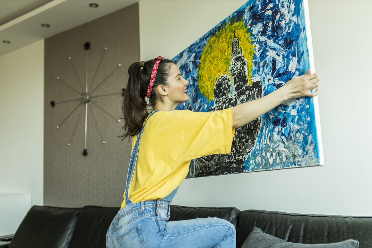 iStock-1311835719 decorate with crafts woman hanging blue and yellow abstract painting on wall