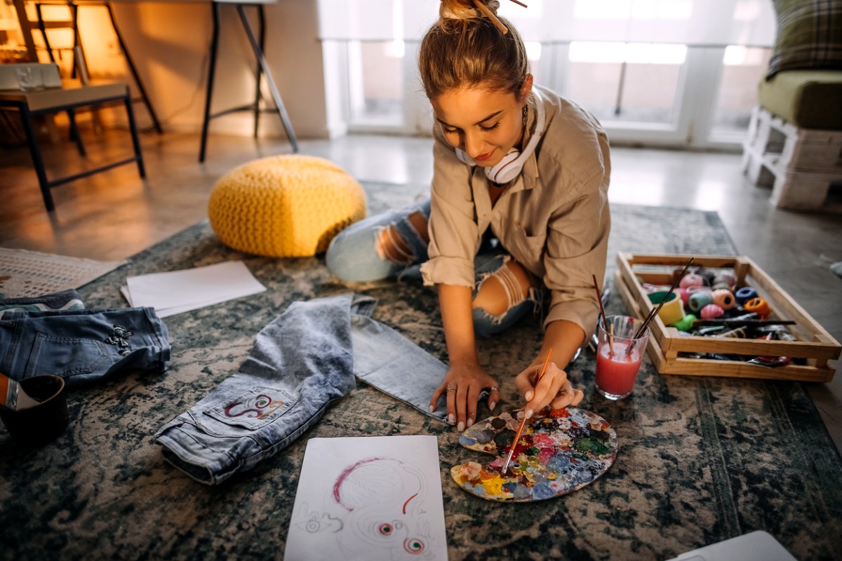 iStock-1354236427 decorating with crafts young woman painting and doing fabric art on denim.