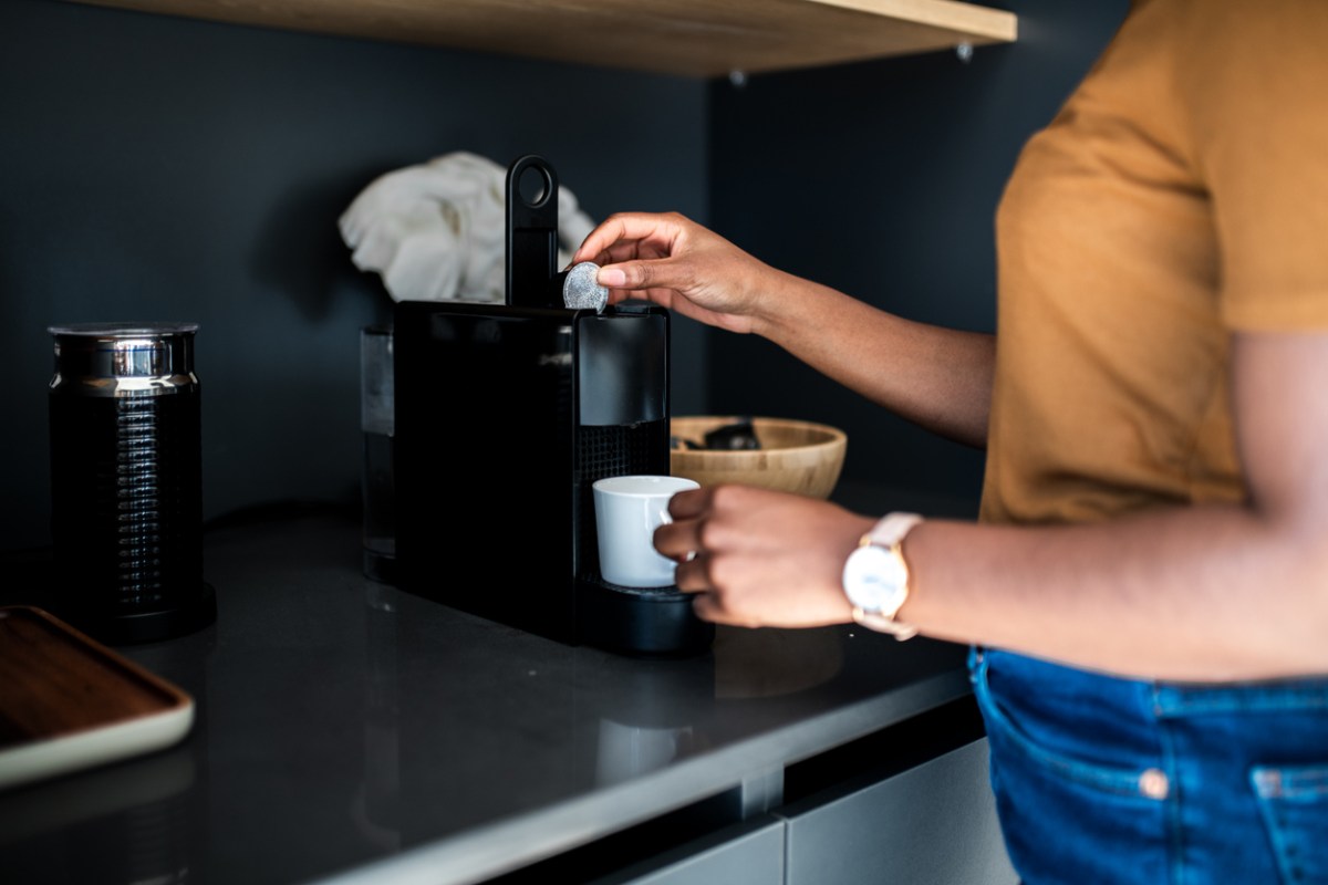 how to clean nespresso machine woman putting pod in coffee machine making coffee