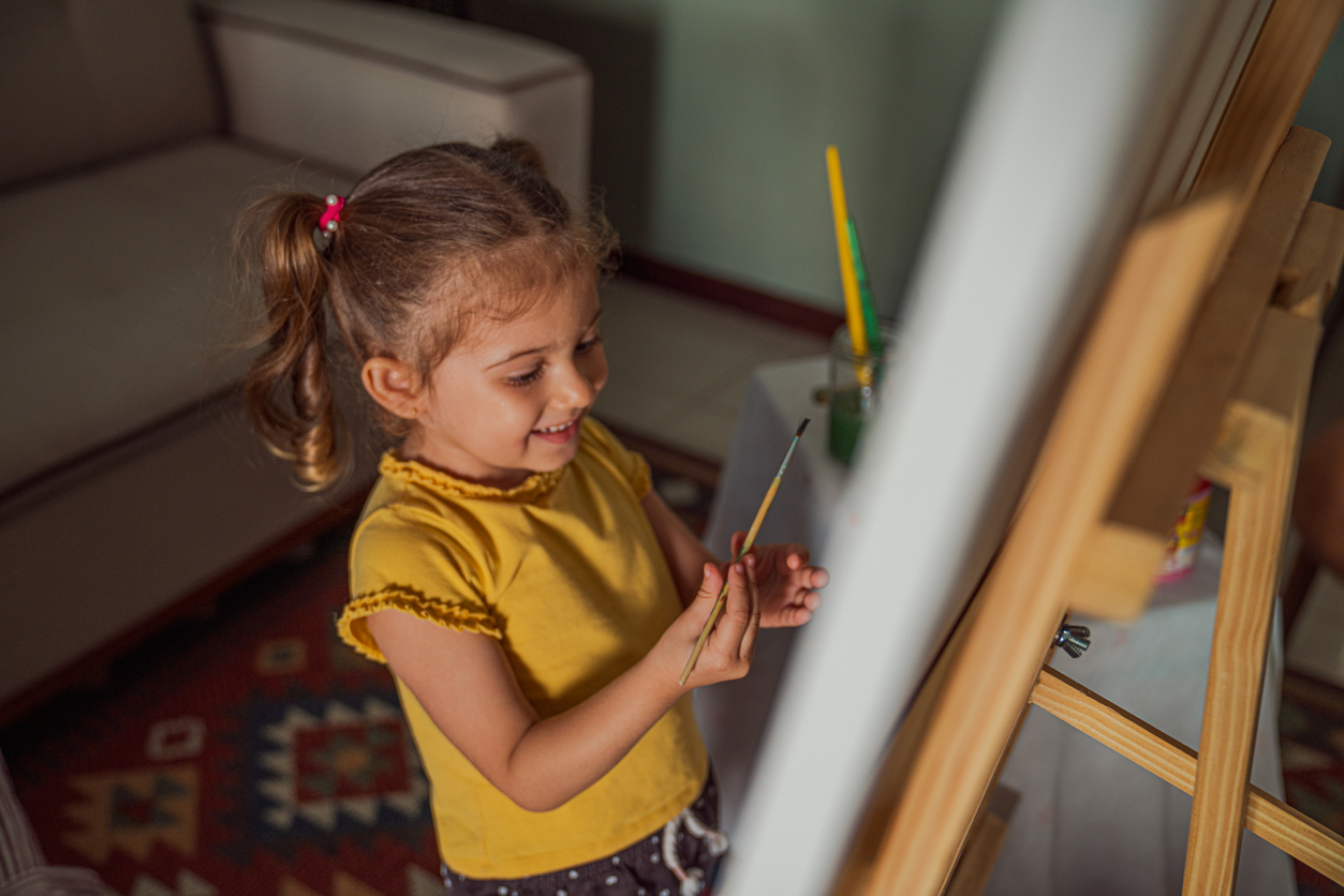 what is a den little girl painting on an easel in den with couch