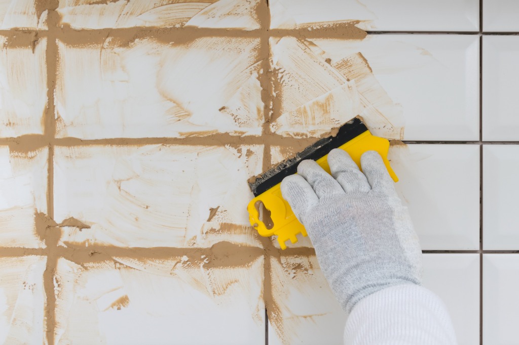 istock 1311119366 how long does grout take to dry close-up-of-a-hand-in-a-protective-glove-holding-a-yellow-spatula-in-the-process-of-grout-of.jpg