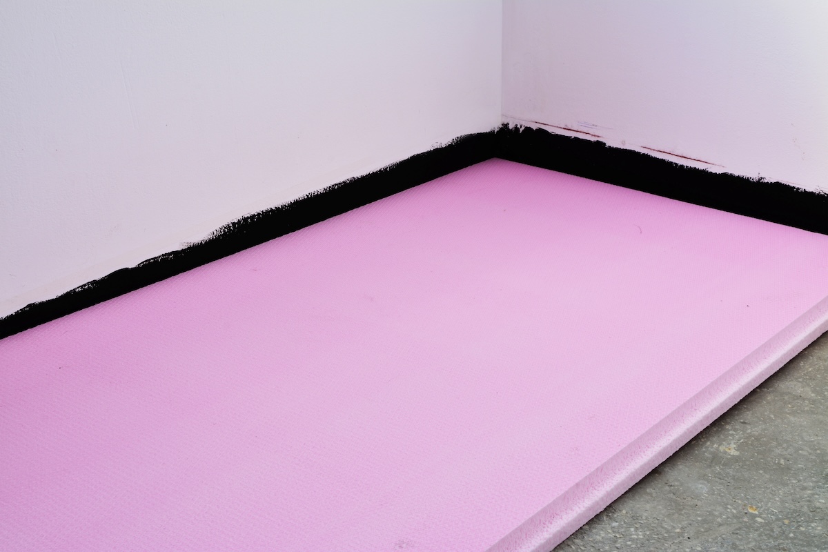 Pink rigid insulation boards on a concrete basement floor.