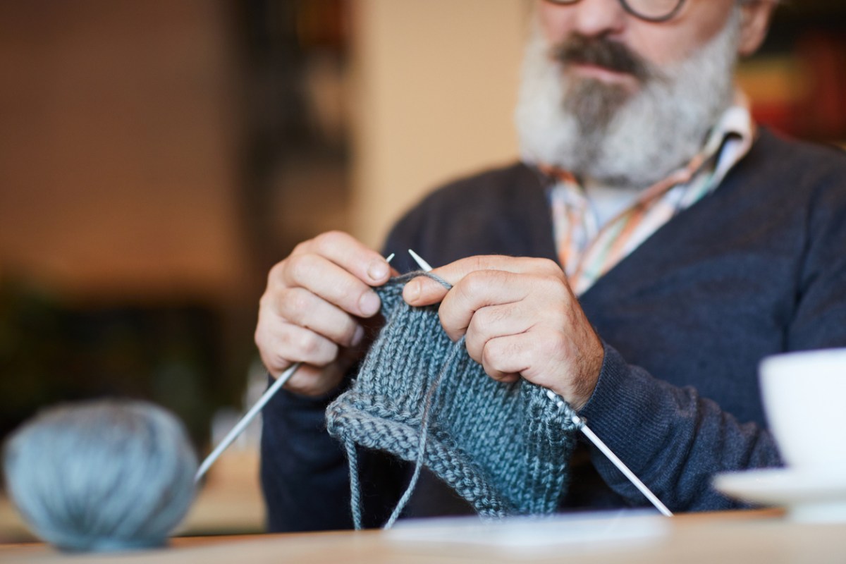 Bearded senior demonstrating a beginner knitting pattern for a scarf or granny square