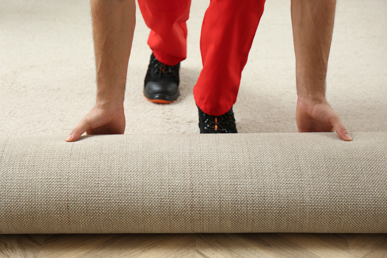 Carpet installer rolling out new carpet on hardwood floor