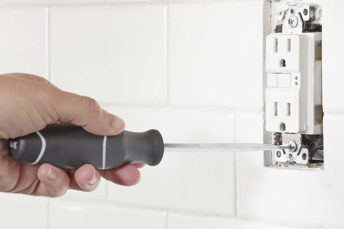 Person uses a screwdriver to install a GFCI electrical outlet into wall.