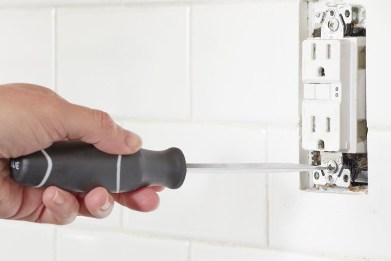 Person uses a screwdriver to install a GFCI electrical outlet into wall.