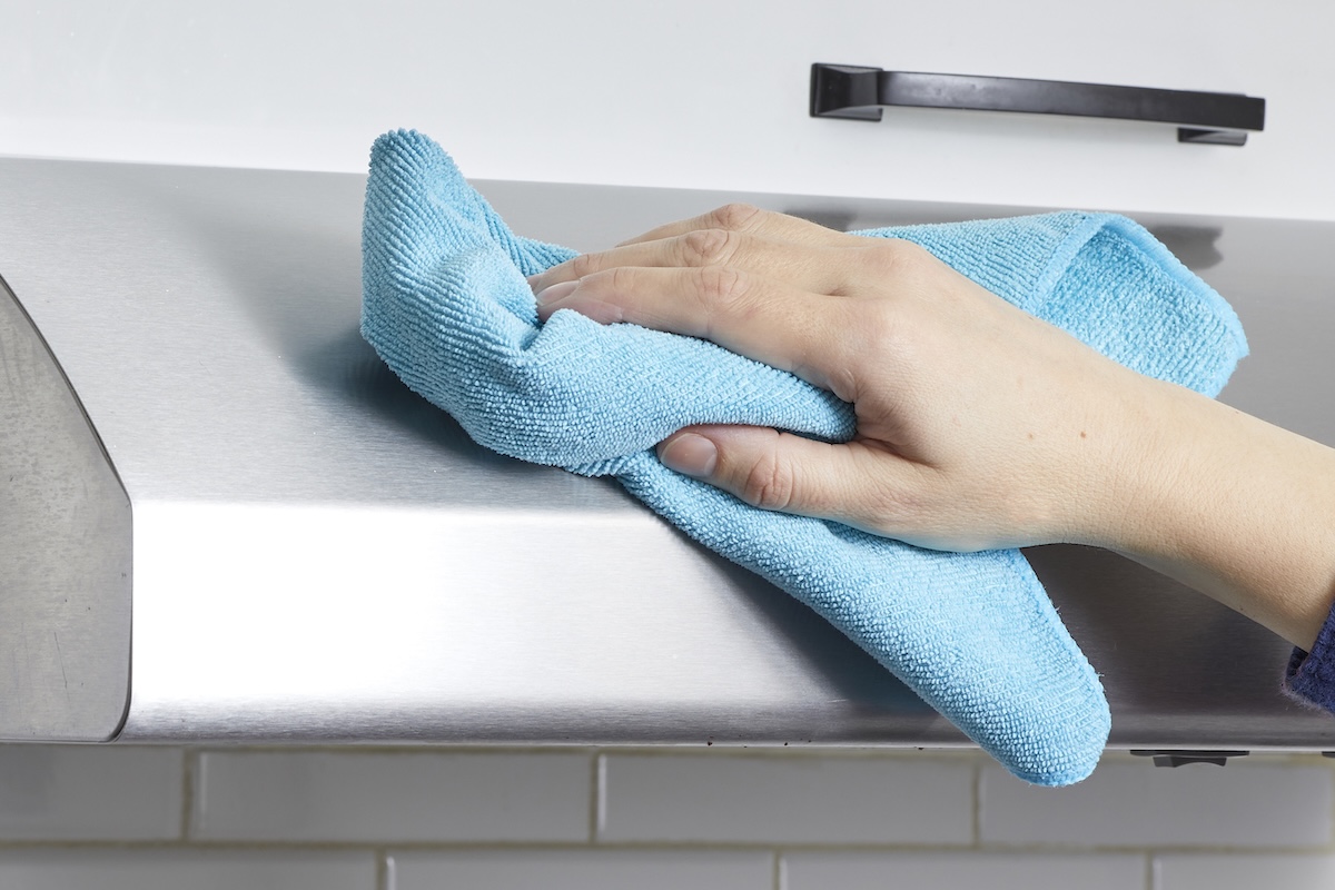 Woman uses a blue microfiber cloth to polish a stainless steel range hood.
