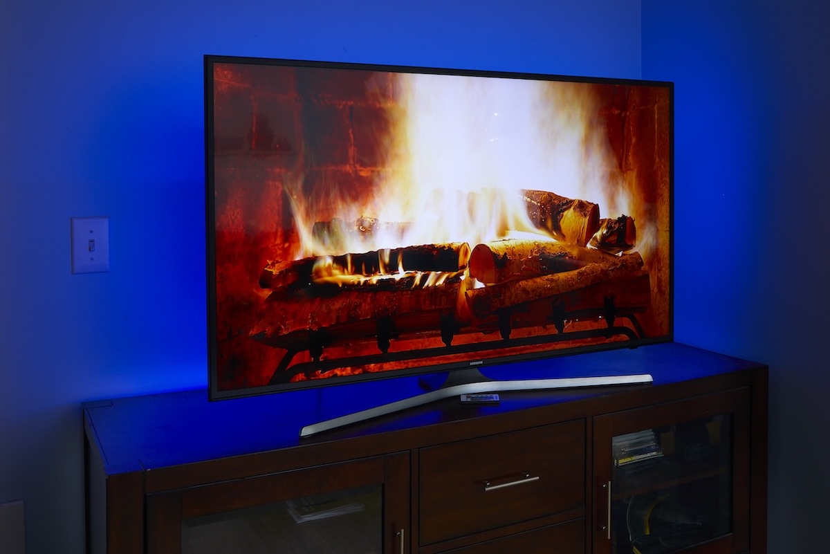 Flat screen TV with image of crackling fireplace, illuminated in blue LED lights in back.