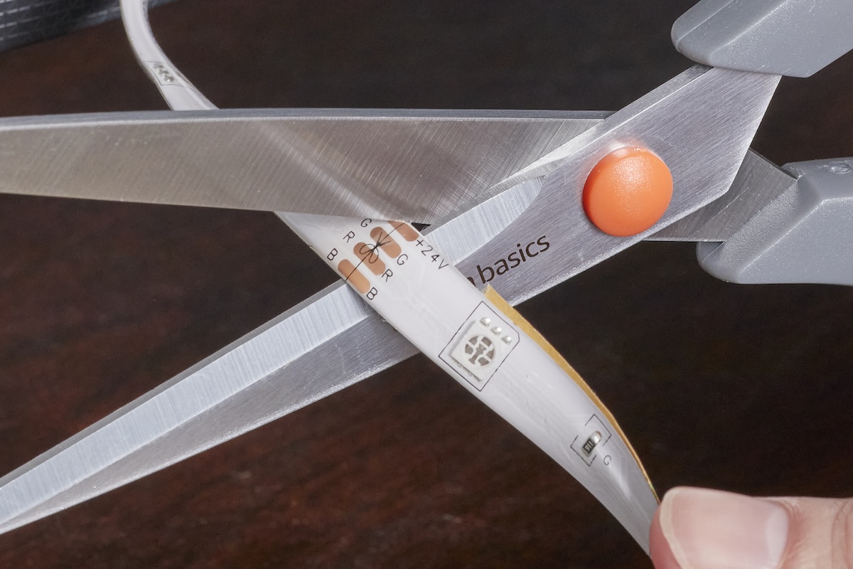 A pair of scissors cutting an LED light strip on the dotted cut line.