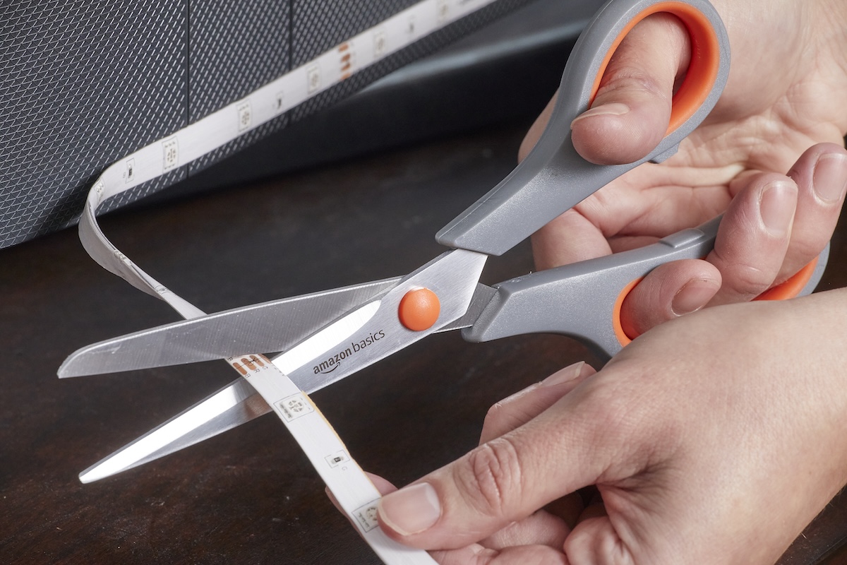 Person uses scissors to cut through LED strip light.