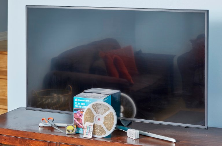Flat-screen TV on cabinet with LED light strip package, scissors, tape measure and other supplies.