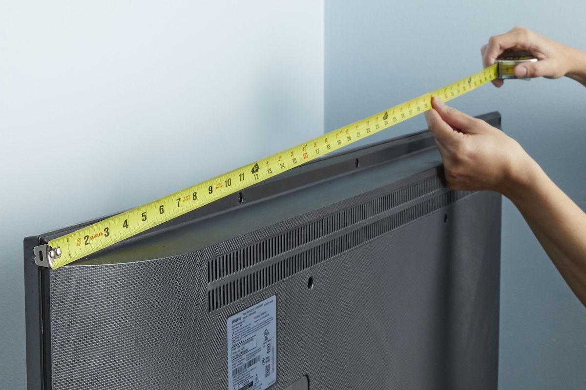 Woman measures the length of the back of a TV using a tape measure.