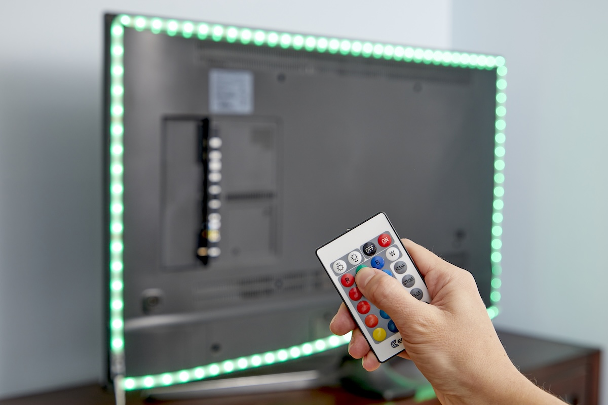 Person uses remote control to illuminate LED lights on the back side of a flat screen TV.