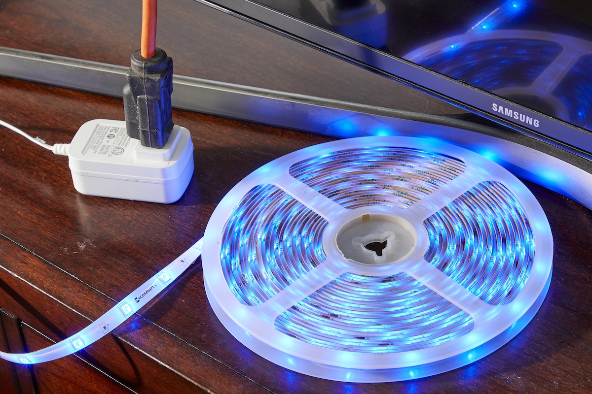 A roll of LED light strip is illuminated blue as it's plugged into an extension cord.