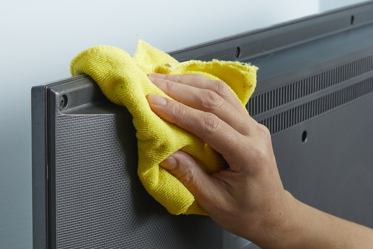Person wipes back of TV screen with a yellow microfiber cloth.