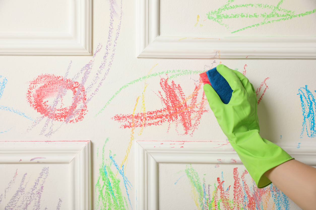 cleaning colorful crayon markings off wall wearing green gloves with sponge