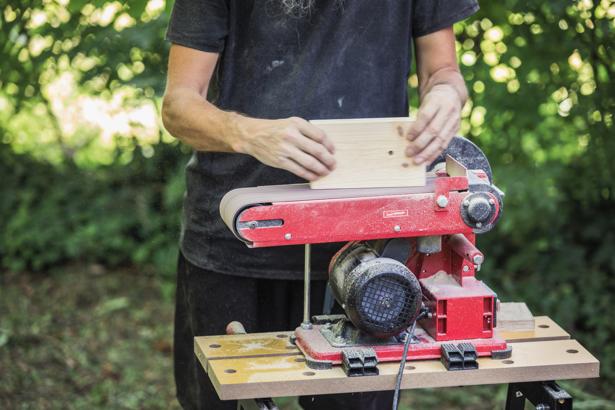 Craftsperson sanding wood block using combination disc belt sander.