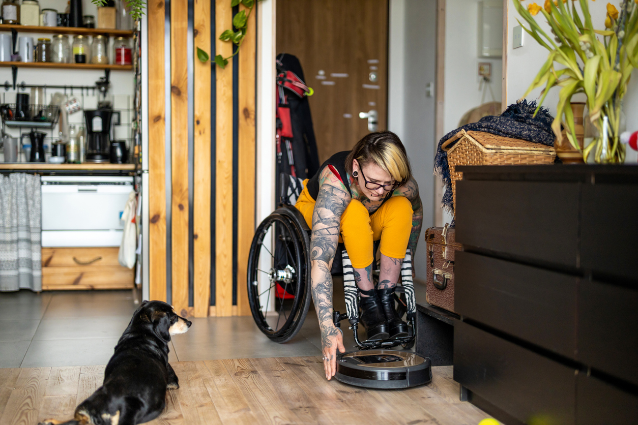 iStock-1396837798 tax refund home improvements Woman in wheelchair adjusting smart robot cleaner