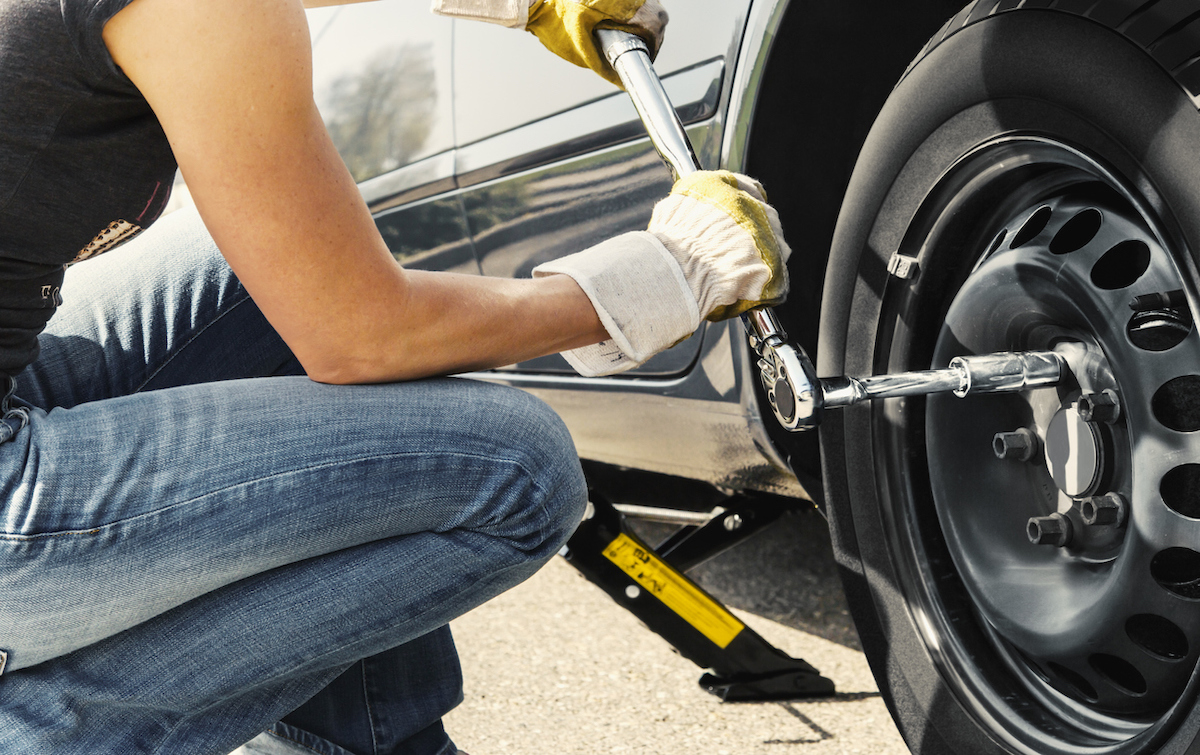 how to use a torque wrench - woman changing tire using torque wrench to tighten lug nuts