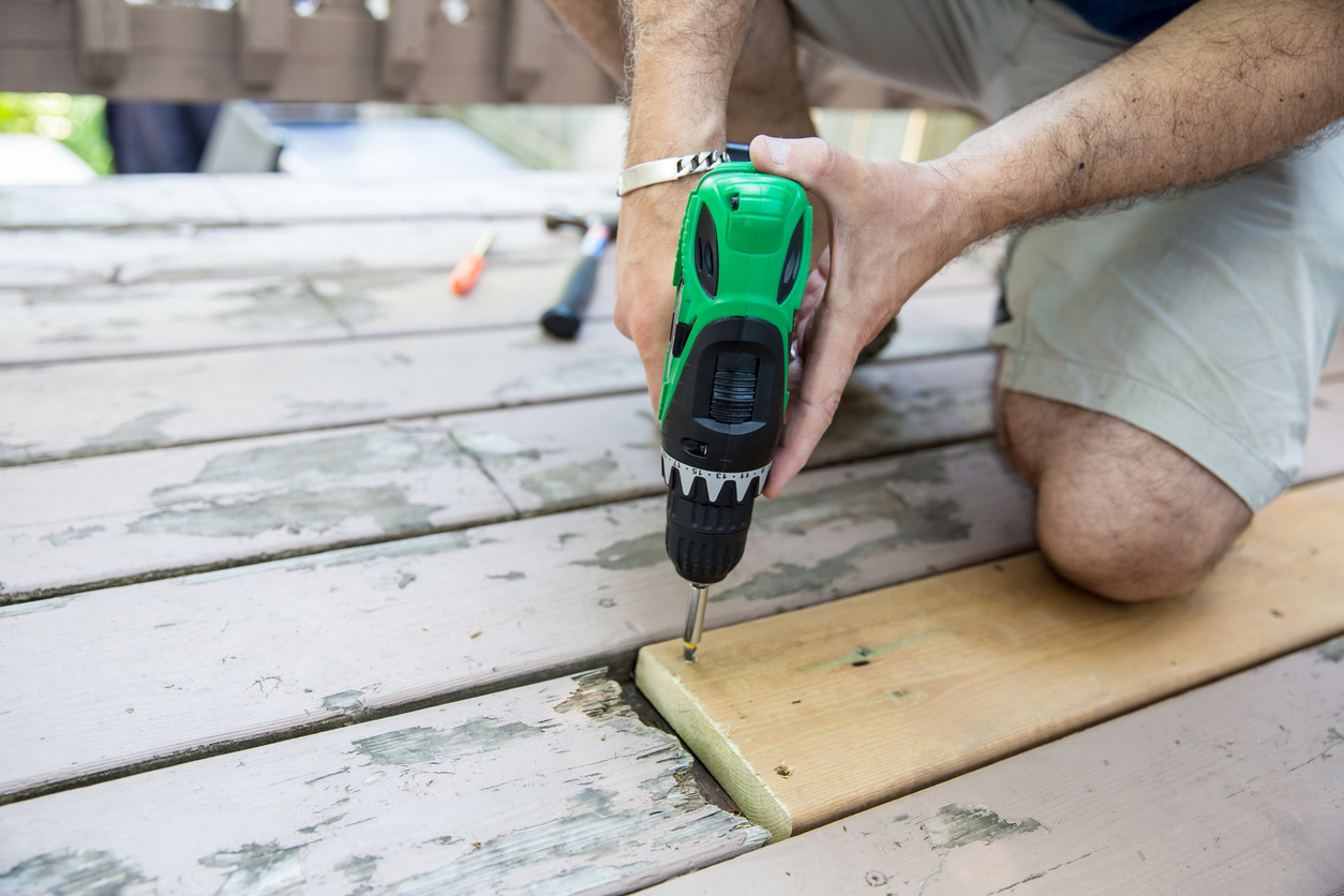 Man drills new deck board into deck alongside older boards.