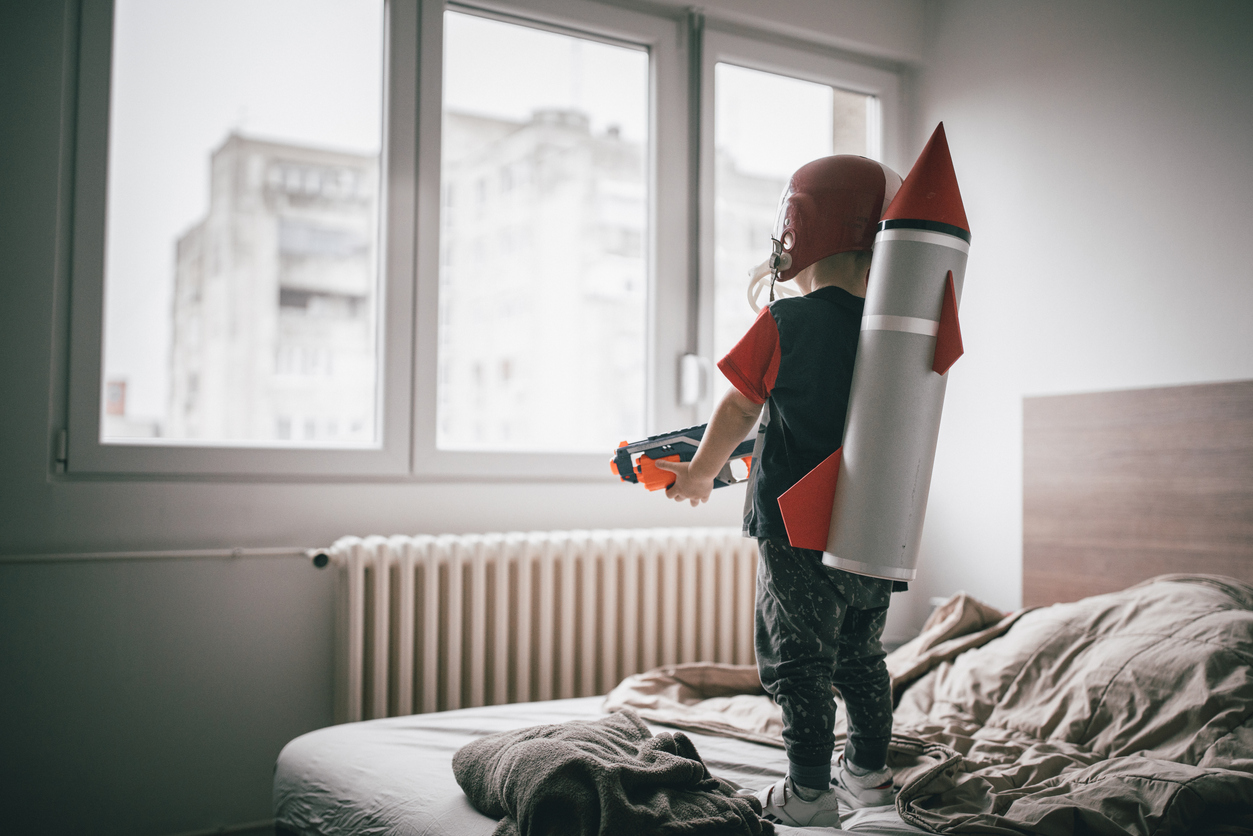 security window film child with space rocket costume and toy gun facing window standing on bed