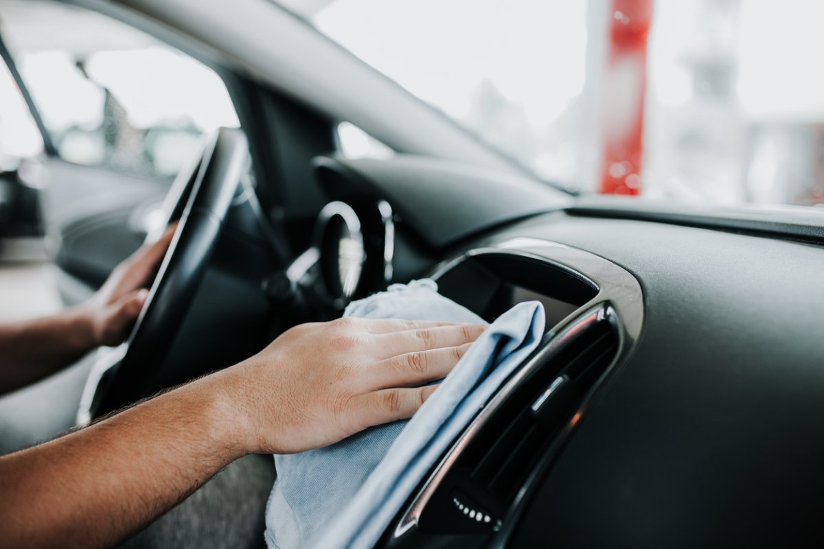 Man wiping down his car dashboard with a blue cloth.