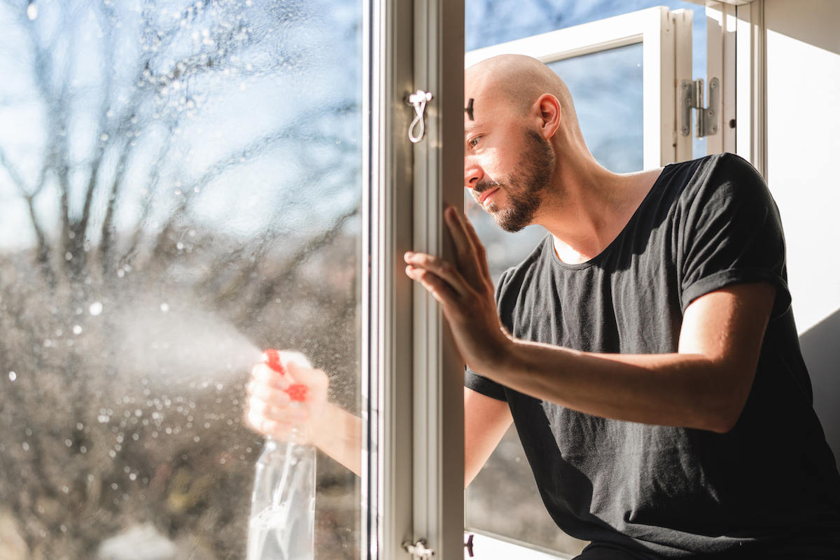 Man sitting in a window sill, leaning out the window to clean its exterior.