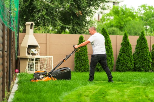A homeowner mowing an overgrown lawn with a push mower.