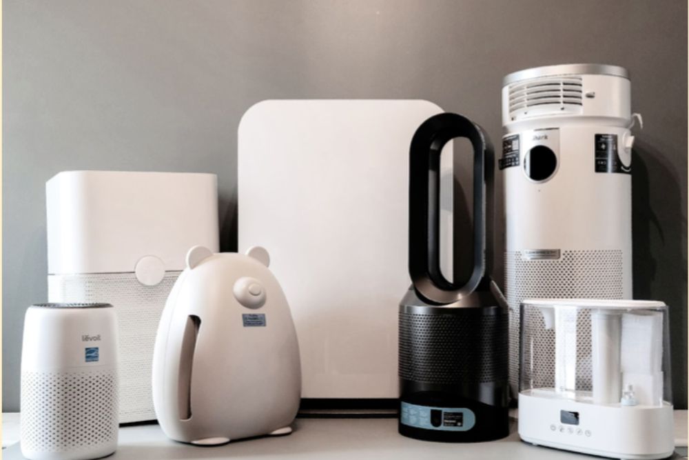 Seven white, gray, and black air purifiers in front of a gray wall