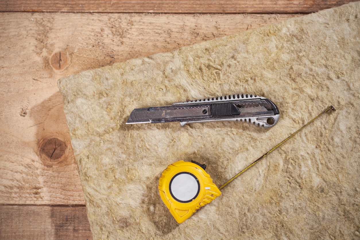 Insulation knife and measuring tape sitting atop mineral wool insulation