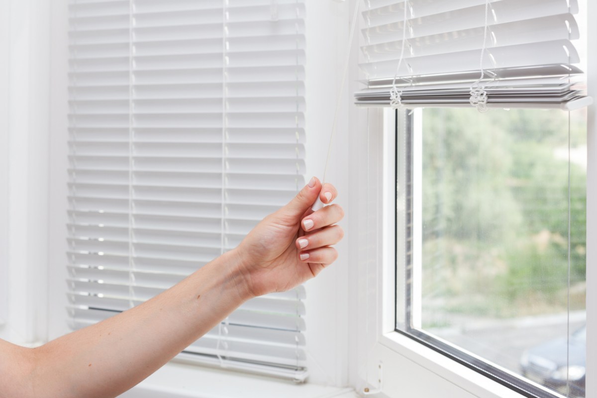 Hand adjusting the height of white mini blinds