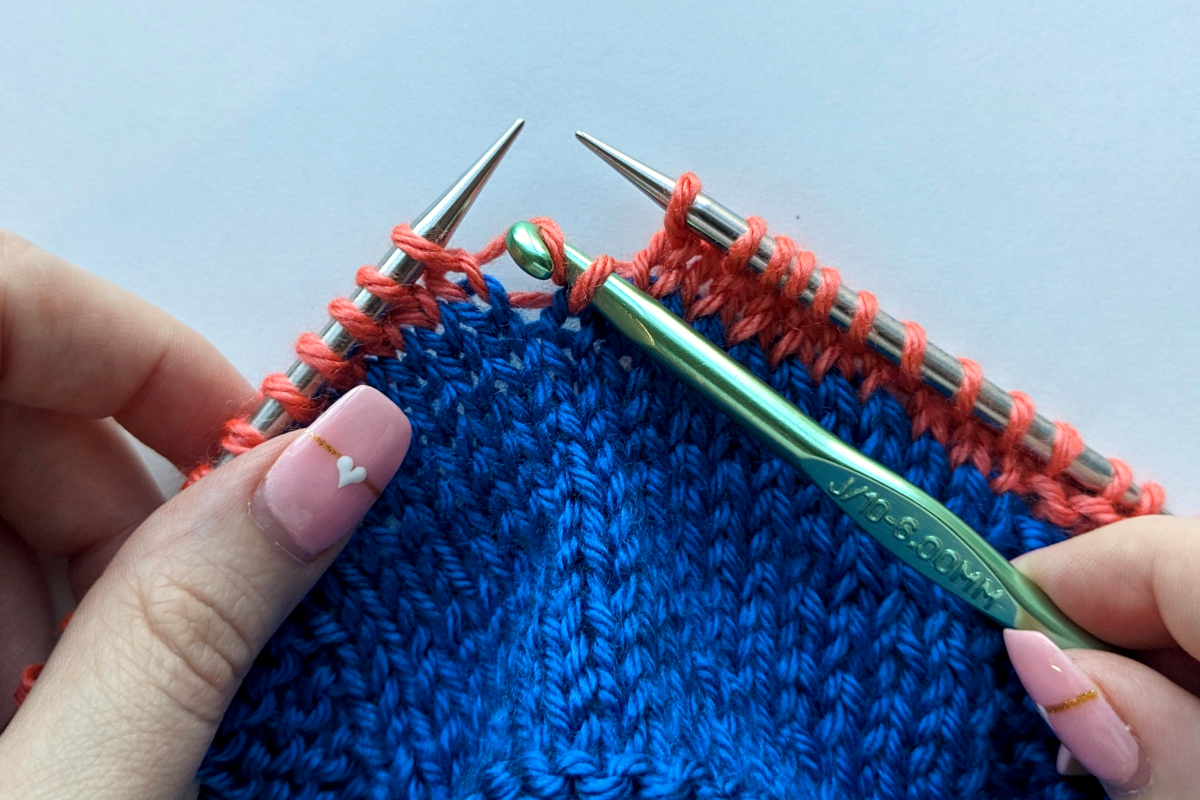 Demonstration of how to fix a dropped stitch in knitting using blue and coral yarn