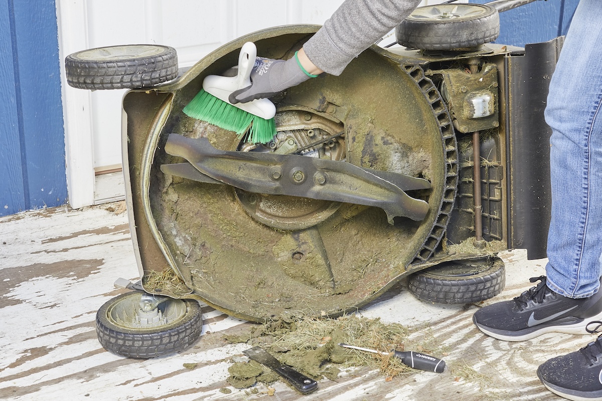 DIYer cleaning the underside of a push lawn mower.