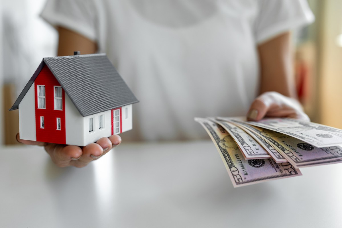 woman holding model home in one hand and a stack of money in the other