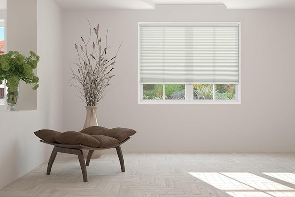 A white room with a small bench and window with honeycomb blinds. 