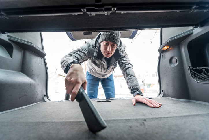 car maintenance tasks - man using vacuum in car trunk