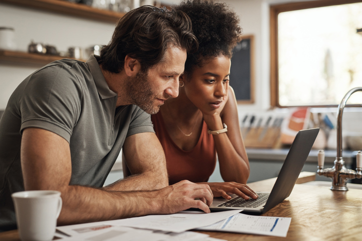 energy-efficient-home-improvement-tax-credits-man-and-woman-looking-at-laptop-in-kitchen-with-papers-on-counter