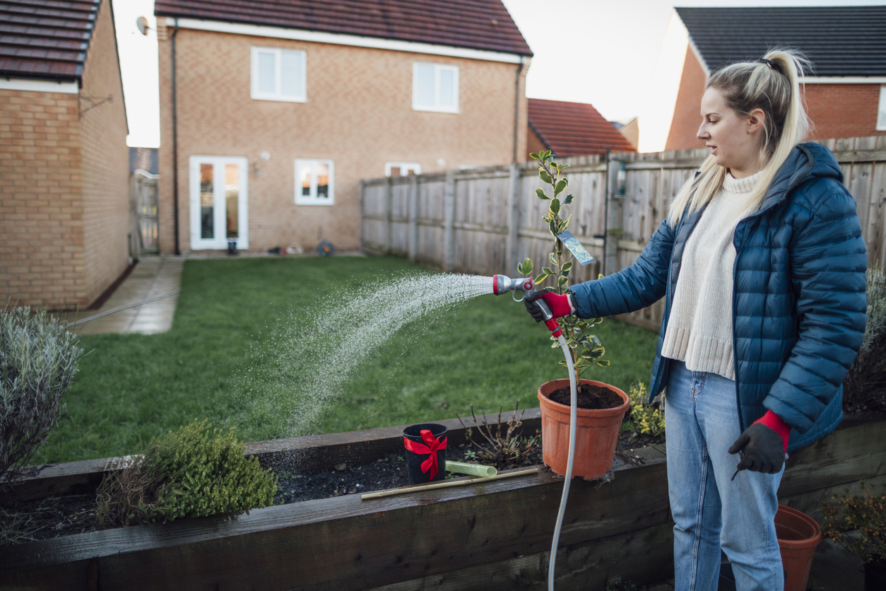 iStock-1295255281 14 Wise Ways to Weatherproof Your Garden woman watering plants in winter coat on cold day