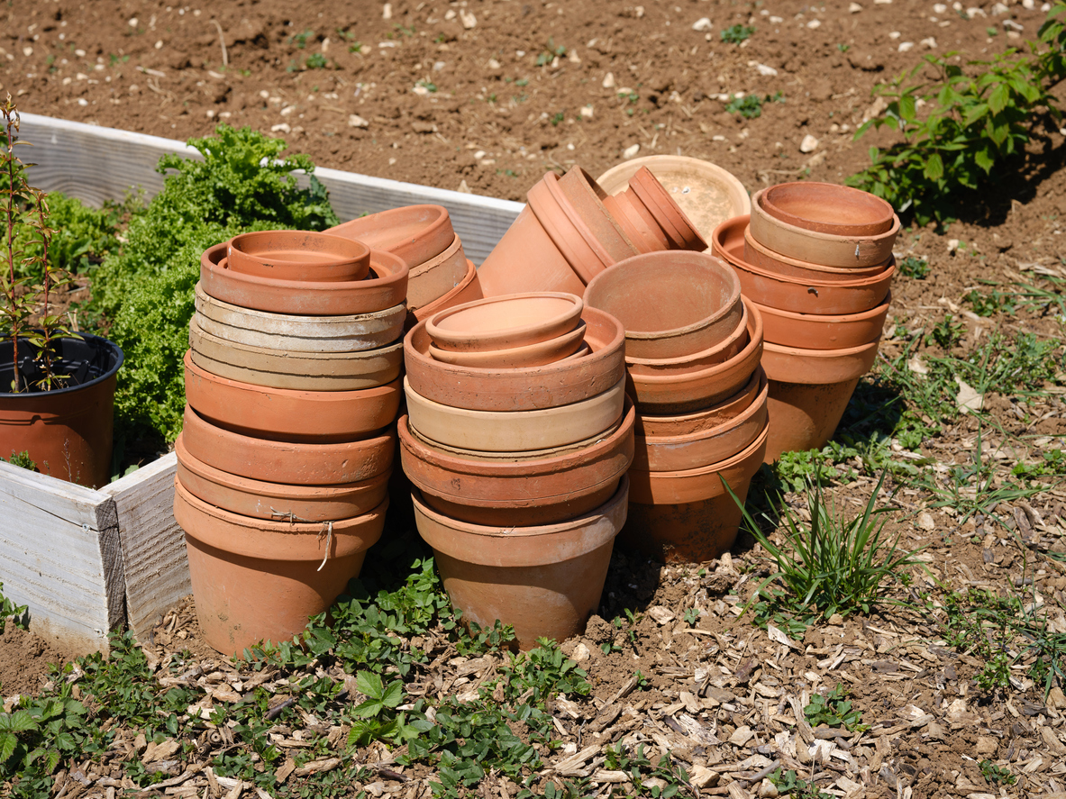 iStock-1314494255 14 Wise Ways to Weatherproof Your Garden pile of terra cotta pots next to planting bed
