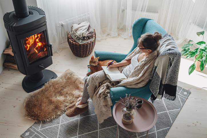 energy-efficient-home-improvement-tax-credit-woman-in-blue-chair-with-cat-in-front-of-wood-burning-stove-in-white-room