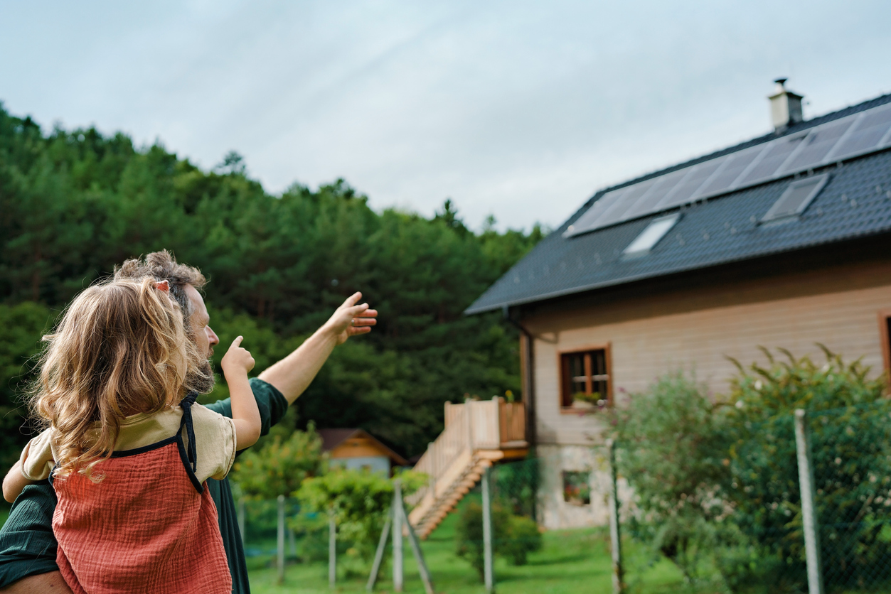 iStock-1431921497 types of paint ear view of dad holding her little girl in arms and showing at their house with installed solar panels