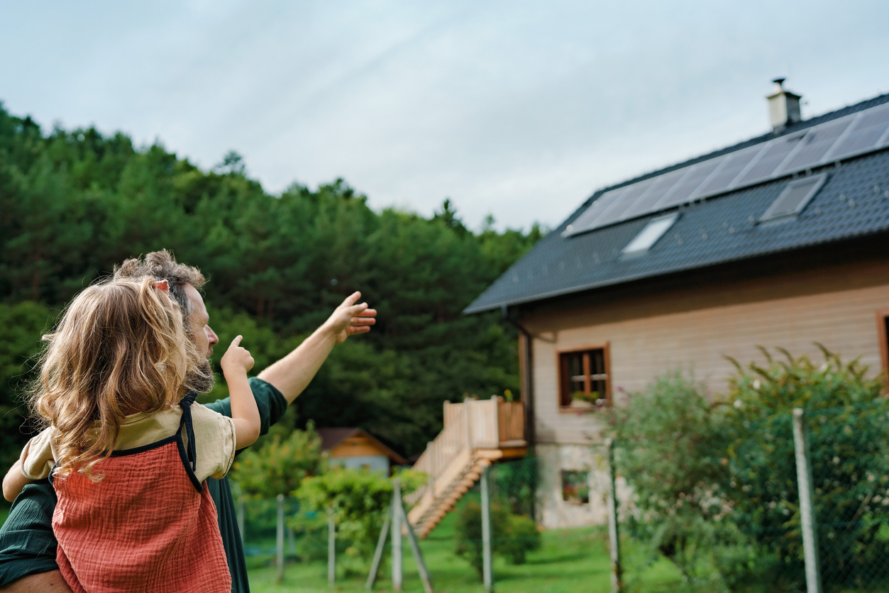 iStock-1431921497 types of paint ear view of dad holding her little girl in arms and showing at their house with installed solar panels