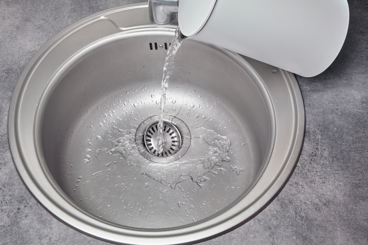iStock-1445283032 how to unclog a sink drain Hot water pours from a white electric kettle into a metal kitchen sink