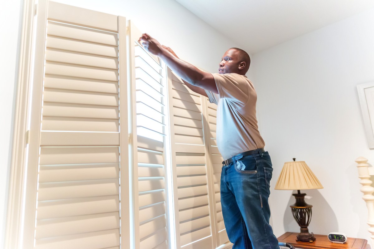iStock-462777985 ways to dress a window Window treatment installer installs wooden shutters
