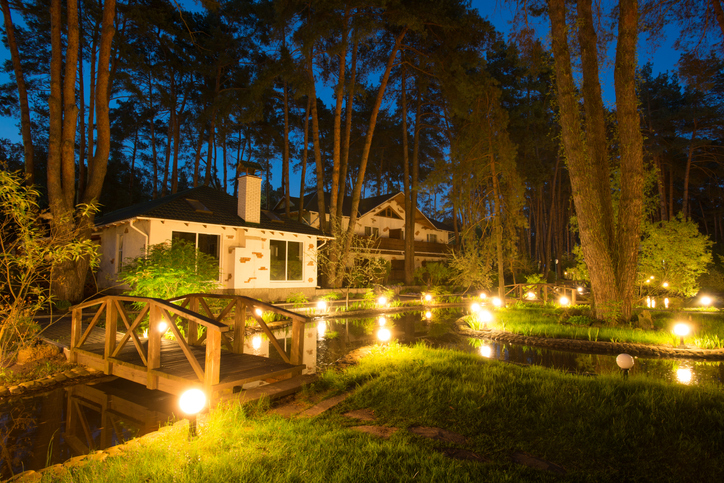 uplighting-landscape-house-with-tall-trees-and-a-pond-with-bridge-at-night